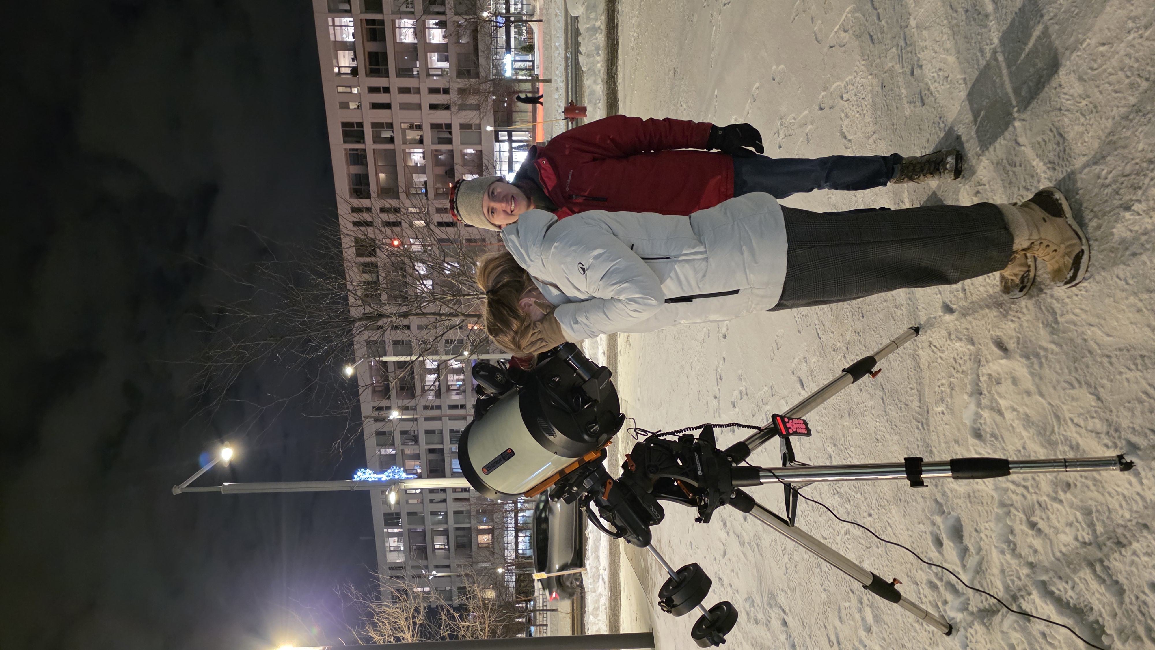 A student looking through a telescope outside on a snowy winter evening.